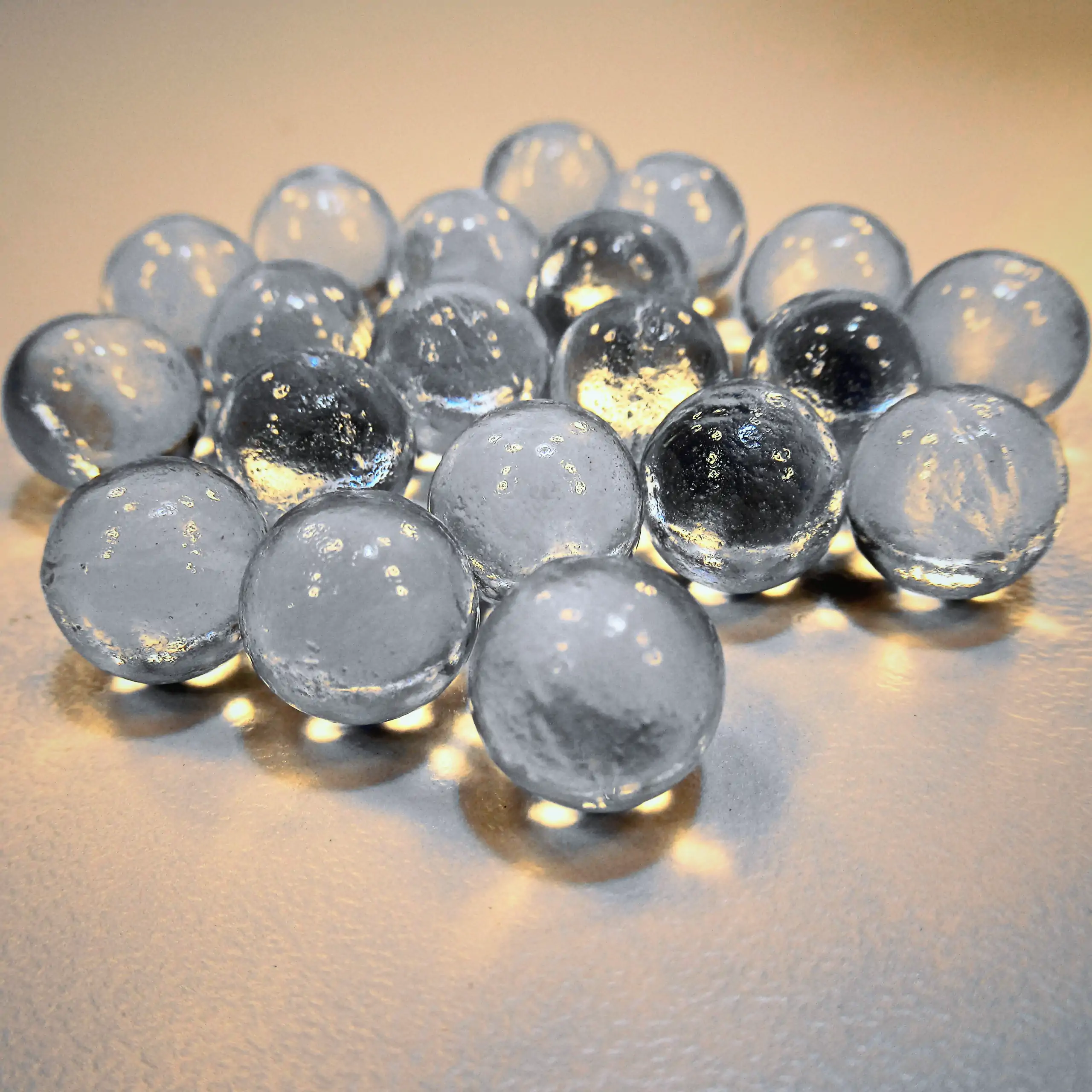 Detailaufnahme der Körrie-Aktiv-Perlen (Glas) / Körrie KAP L: Eine kleine Gruppe leuchtend transparenter, glänzender, gehärteter Glasperlen, verstreut auf einer hellen Oberfläche mit funkelnden Lichtreflexen für einen kristallklaren, realistisch-natürlich