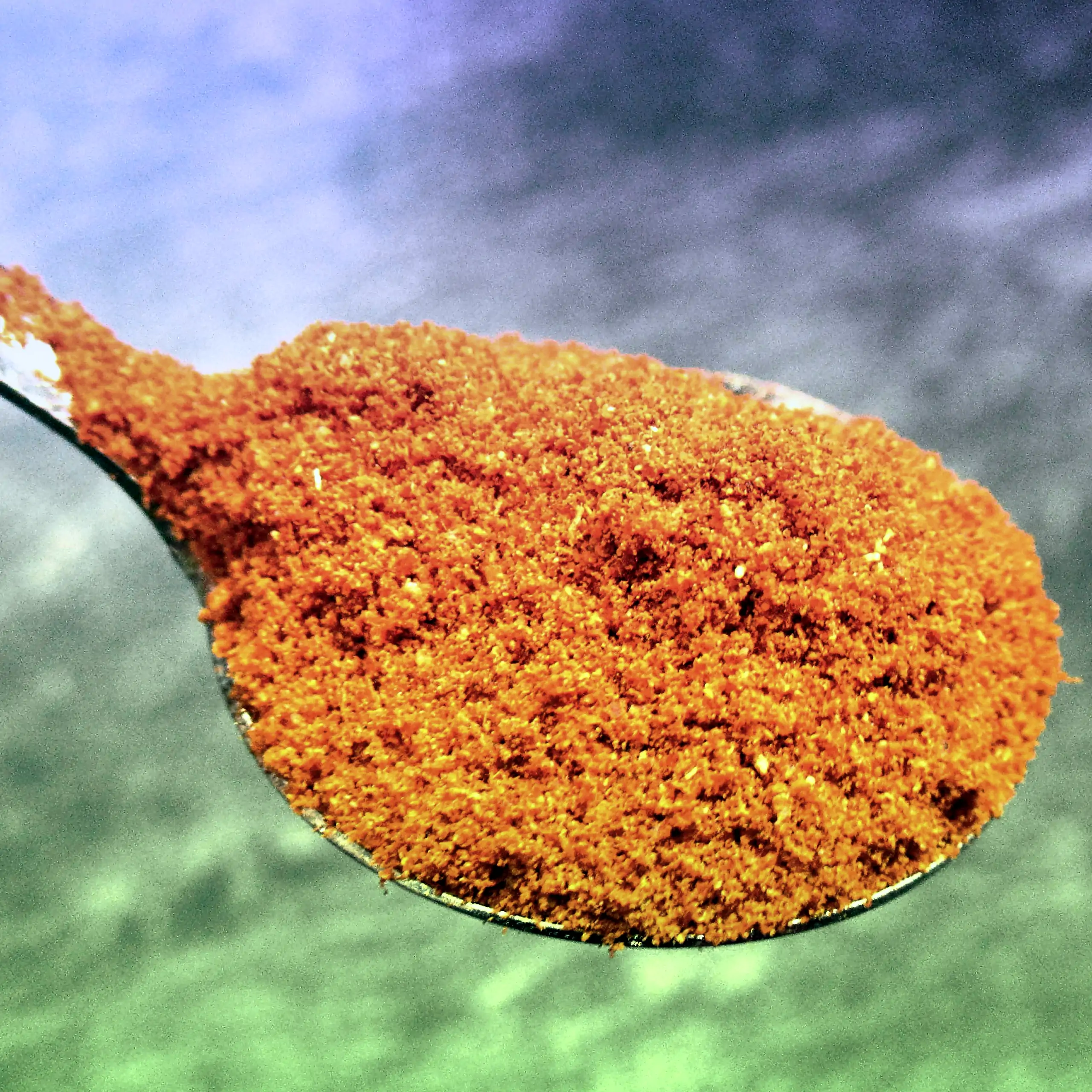 Zusätzliches Bild der Körrie 8zB Gewürzmischung: Ein Löffel voller leuchtend-roter, fein gemahlener Gewürzmischung auf grün-blauem Hintergrund, der die intensive, feurige Textur und scharfe Nuance betont. Diese hochwertige, vegane und salzfreie Gewürzmisc