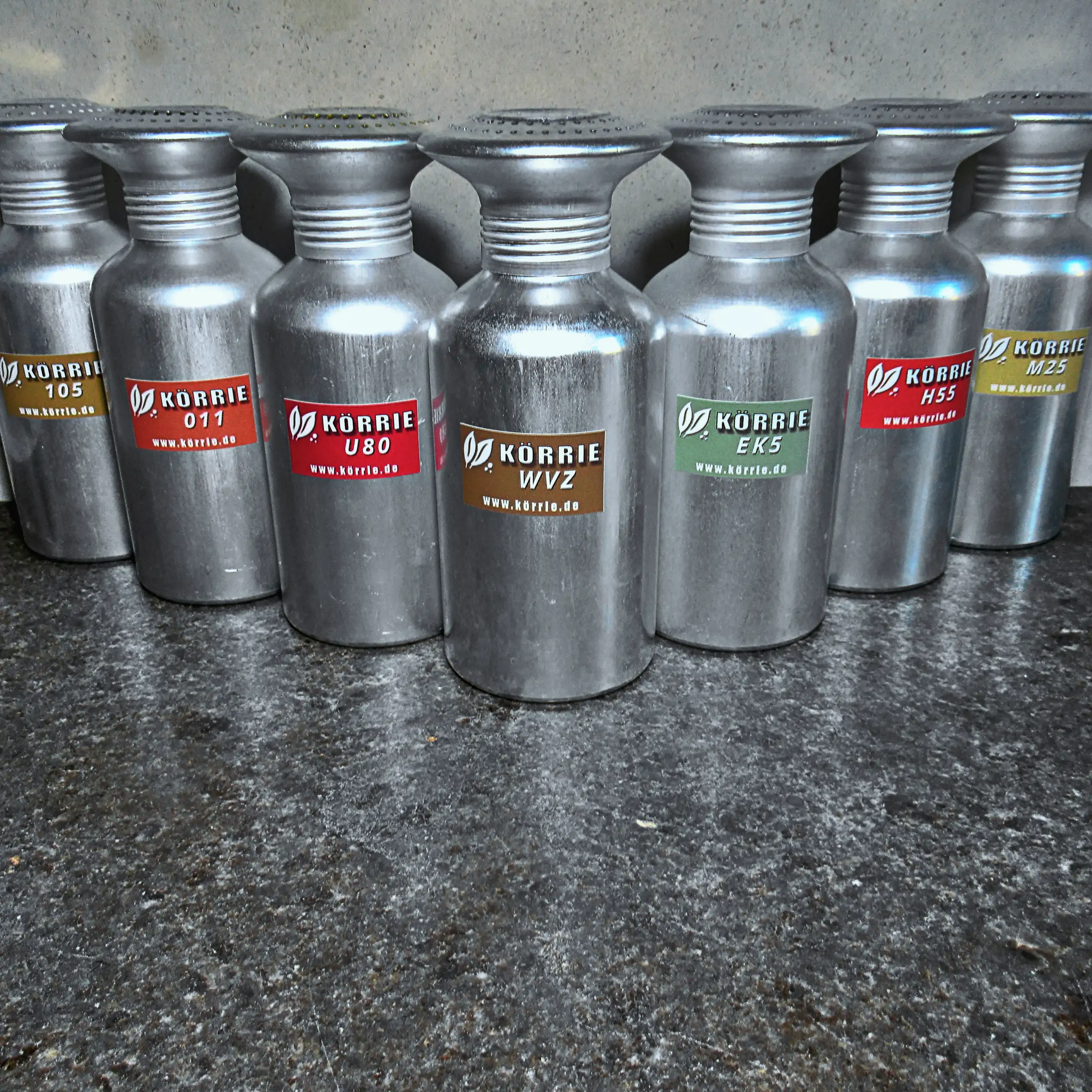 Zusätzliches Bild des Körrie-Gewürz-Streuer: Eine Reihe von robusten, silberfarbenen Metallstreuern mit perforierten Deckeln, beschriftet mit Etiketten verschiedener Körrie-Varianten wie "Körrie 105", "Körrie 011", "Körrie U80", "Körrie WVZ", "Körrie EK5"