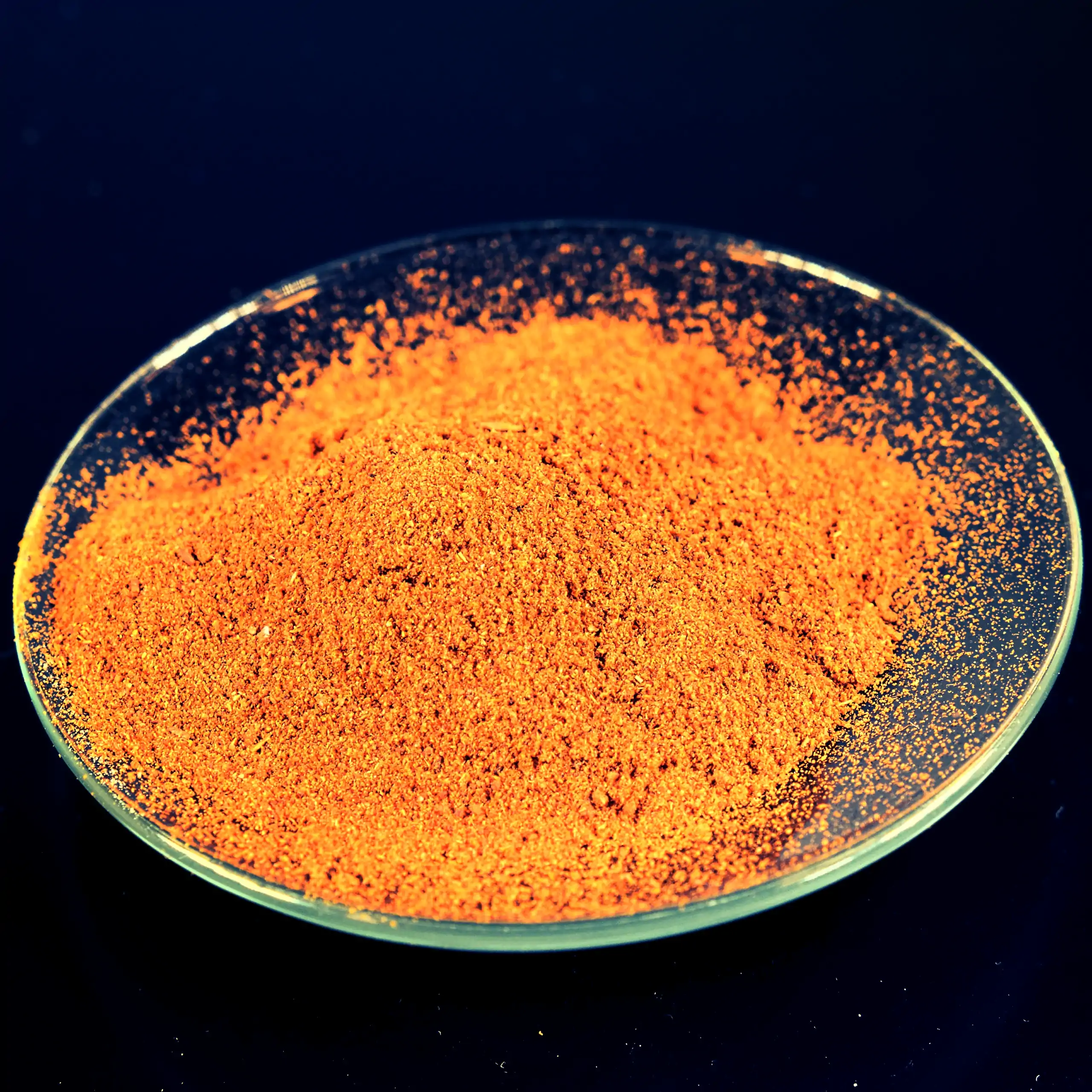 Detailaufnahme der Körrie 8zB Gewürzmischung: Ein Haufen leuchtend roter, fein gemahlener, aromatischer Gewürzmischung in einer transparenten Glasschale auf dunklem Hintergrund, die intensive, feurige Textur und scharfe Nuance betonend, für einen Appetit 