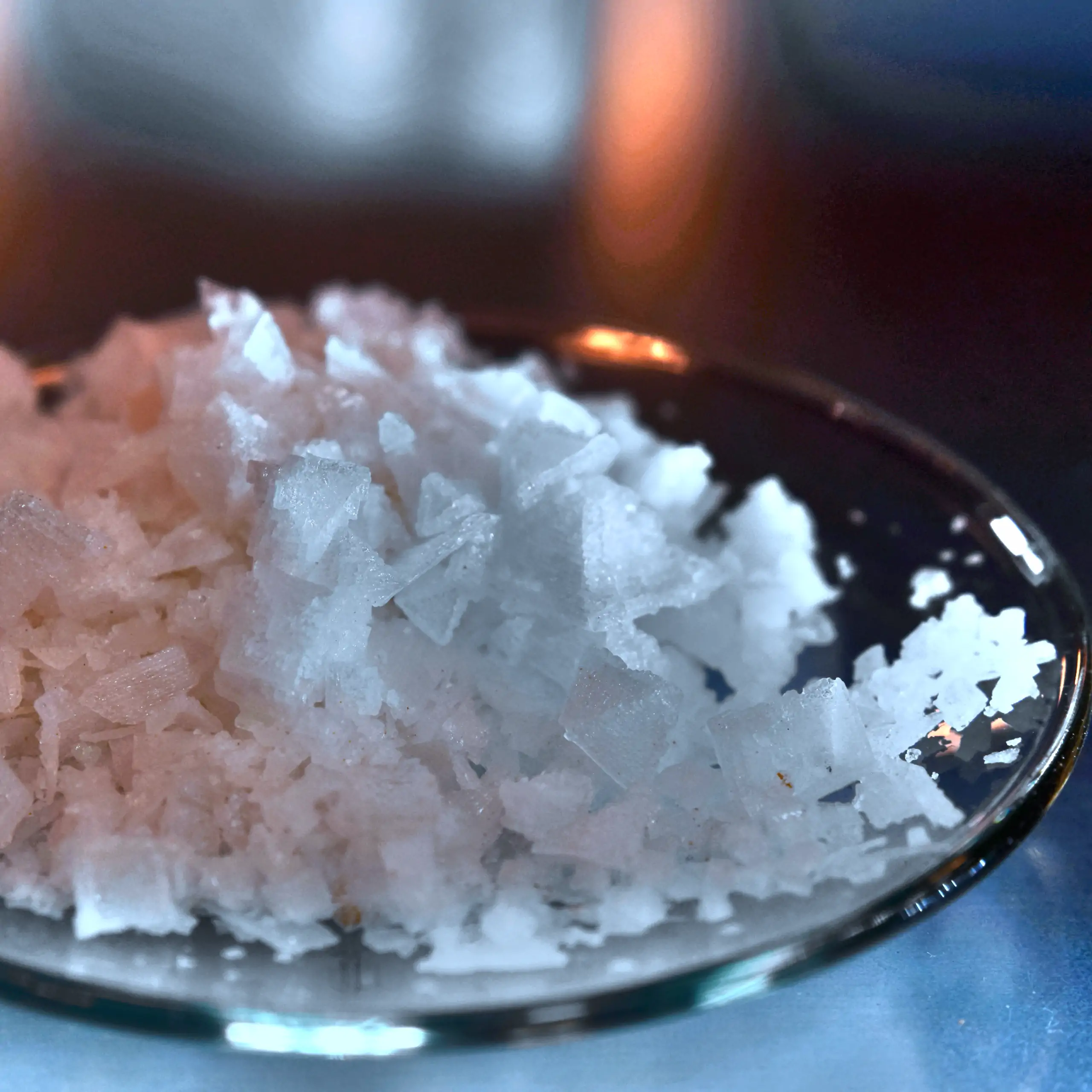 Alternatives Vorschaubild der Galerie für Fleur de Sel (Pyramidensalz): Ein Haufen leuchtend weißer, knusprig-pyramidenförmiger Salzflocken, kunstvoll auf einem transparenten Glas-Teller arrangiert, präsentiert in einer Nahaufnahme für einen frischen, kri