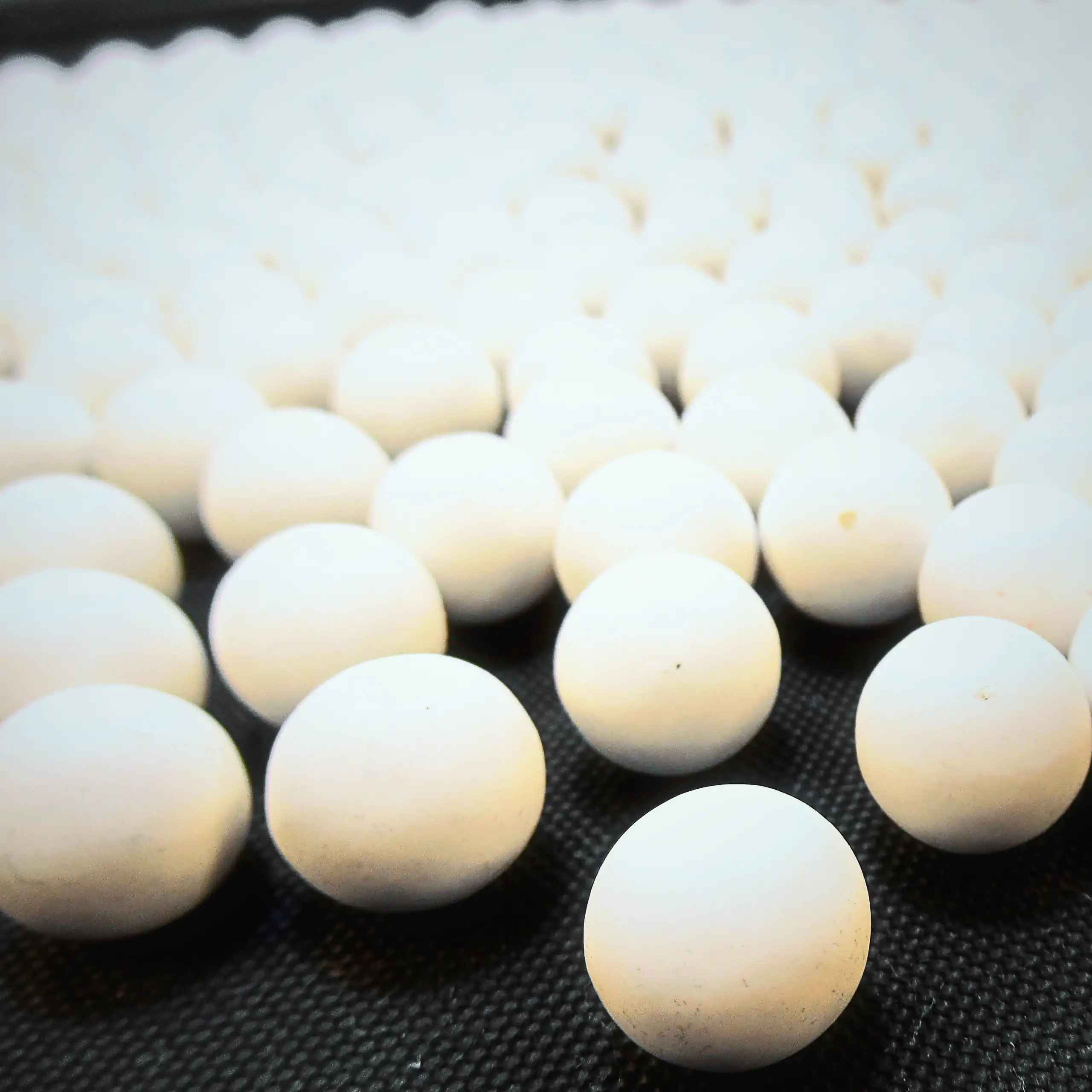 Detailaufnahme der Körrie-Aktiv-Perlen (Keramik) / Körrie KAP S: Eine Gruppe leuchtend weißer, matter, runder Keramikperlen aus Aluminiumoxid, verstreut auf einer dunklen Oberfläche für eine reine, funktionale Darstellung. Diese hochwertigen Aktiv-Perlen 