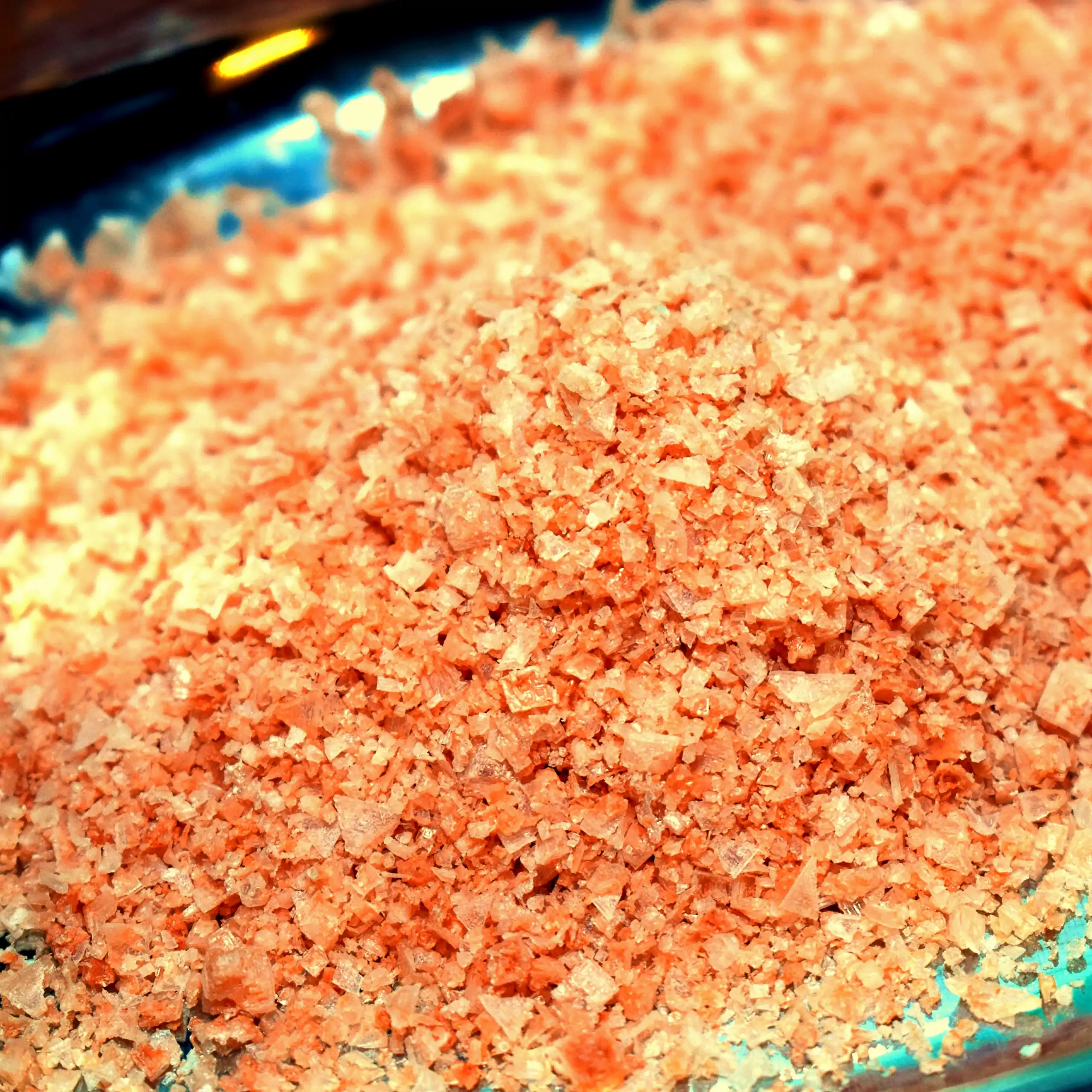 Ergänzende Ansicht der rosa Salzflocken: Ein Haufen leuchtend rosa, knusprig-flockiger Salzmischung in einer transparenten Glasschale auf blauem Hintergrund, der die mineralreiche, kristalline Textur und natürliche Färbung betont für einen frischen, appet