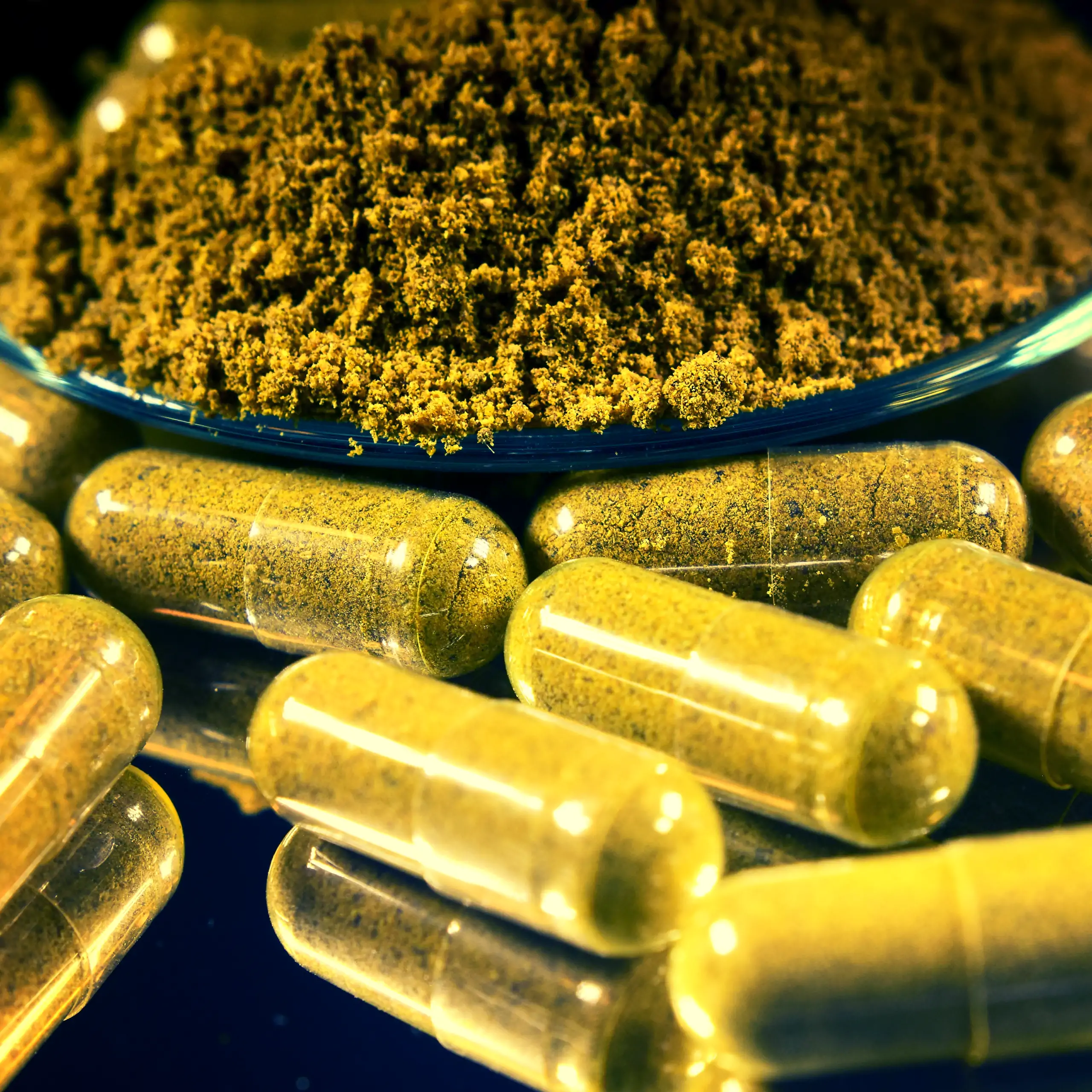 Detailaufnahme der Körrie 105 Kapseln / des Körrie 105K: Eine Nahaufnahme von leuchtend gelben, transparenten veganen Kapseln, gefüllt mit fein gemahlener goldgelber Gewürzmischung, ergänzt durch einen Haufen des Pulvers in einer Schale auf dunklem Hinter