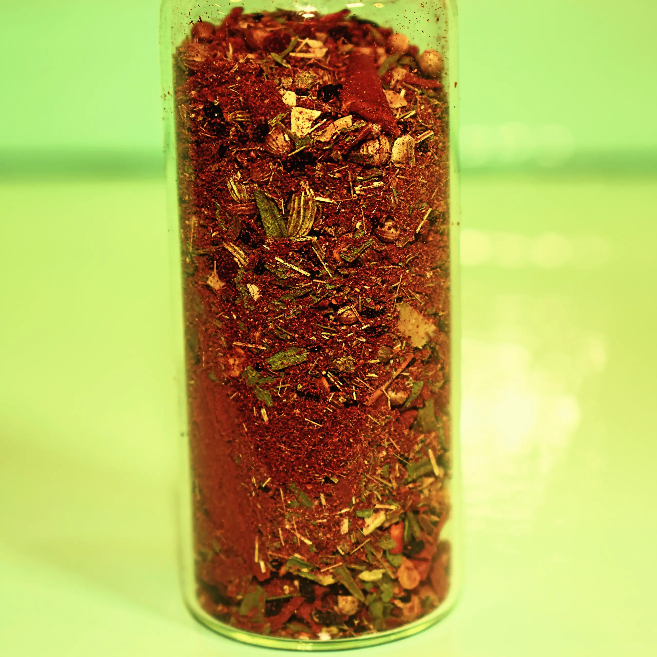 Zusätzliches Bild der herzhaften Gewürzmischung Körrie FLY: Eine transparente Glasflasche gefüllt mit farbenfroher, grob geflockter Kräuter- und Gewürzmischung, die rote Chili- und Paprikflocken, grüne Kräuter, gelbe Samen und Saaten, schwarze Nigella-Sam