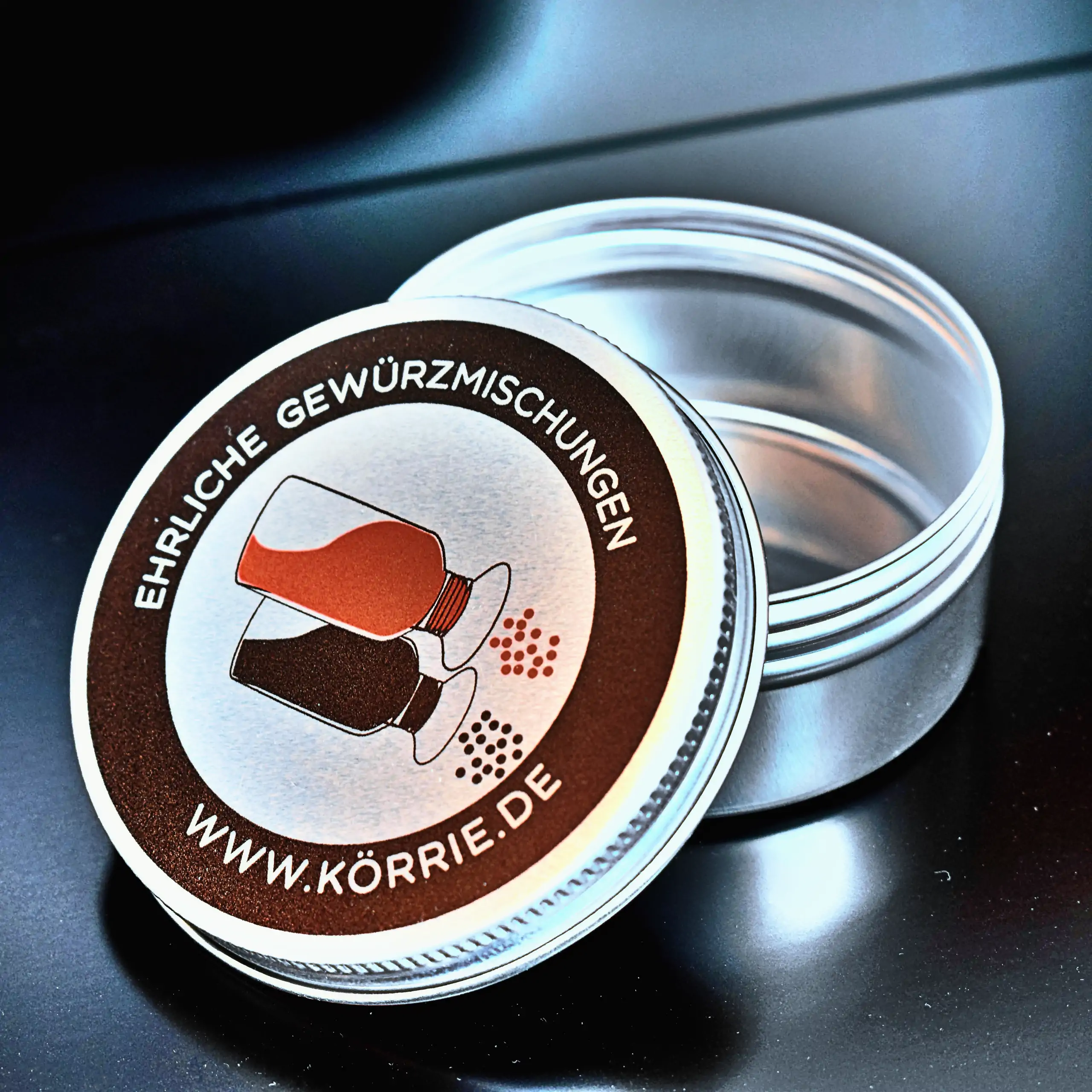 Alternatives Vorschaubild der Galerie für Körrie-Support-Dose / Körrie KSD: Eine runde, kompakte Metall-Dose mit schwarzem Rand und bedrucktem Schraubdeckel, der auf der geöffneten Dose seitlich aufliegt. Auf dem Deckel das ikonische Logo von Körrie mit z