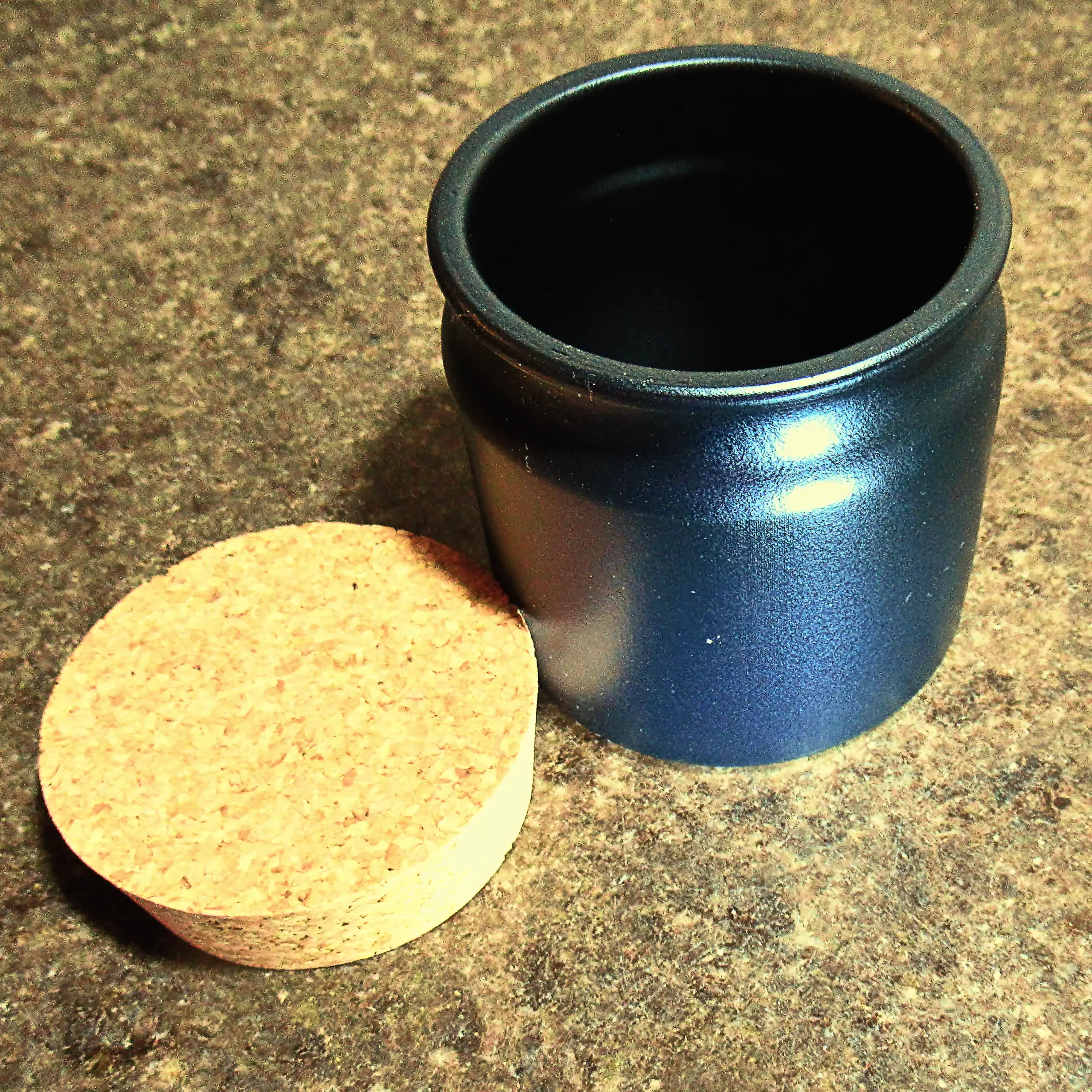 Alternatives Vorschaubild der Galerie für Körrie-Keramik-Töpfchen / Körrie KKT: Ein elegantes, mattschwarzes Keramikgefäß mit natürlichem Korkverschluss, offen präsentiert mit dem Korken daneben auf einer Küchenarbeitsplatte aus seidenmatt poliertem Jura-