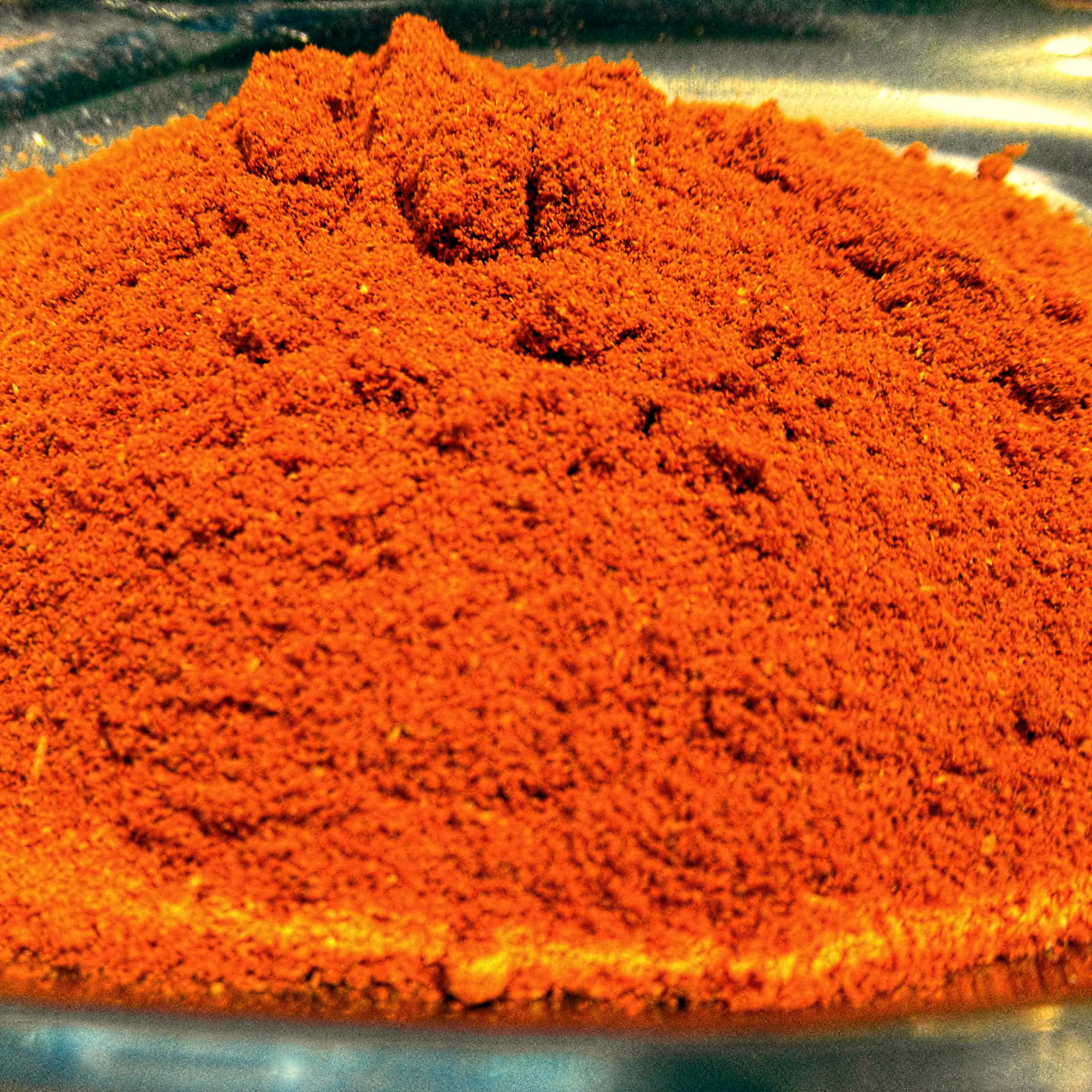 Ergänzende Ansicht der Körrie 8zB Gewürzmischung: Ein Haufen leuchtend roter, fein gemahlener, aromatische Gewürzmischung in einer metallischen Schale auf dunklem Hintergrund, der die intensive, feurige Textur und scharfe Nuance betont, für einen appetitl