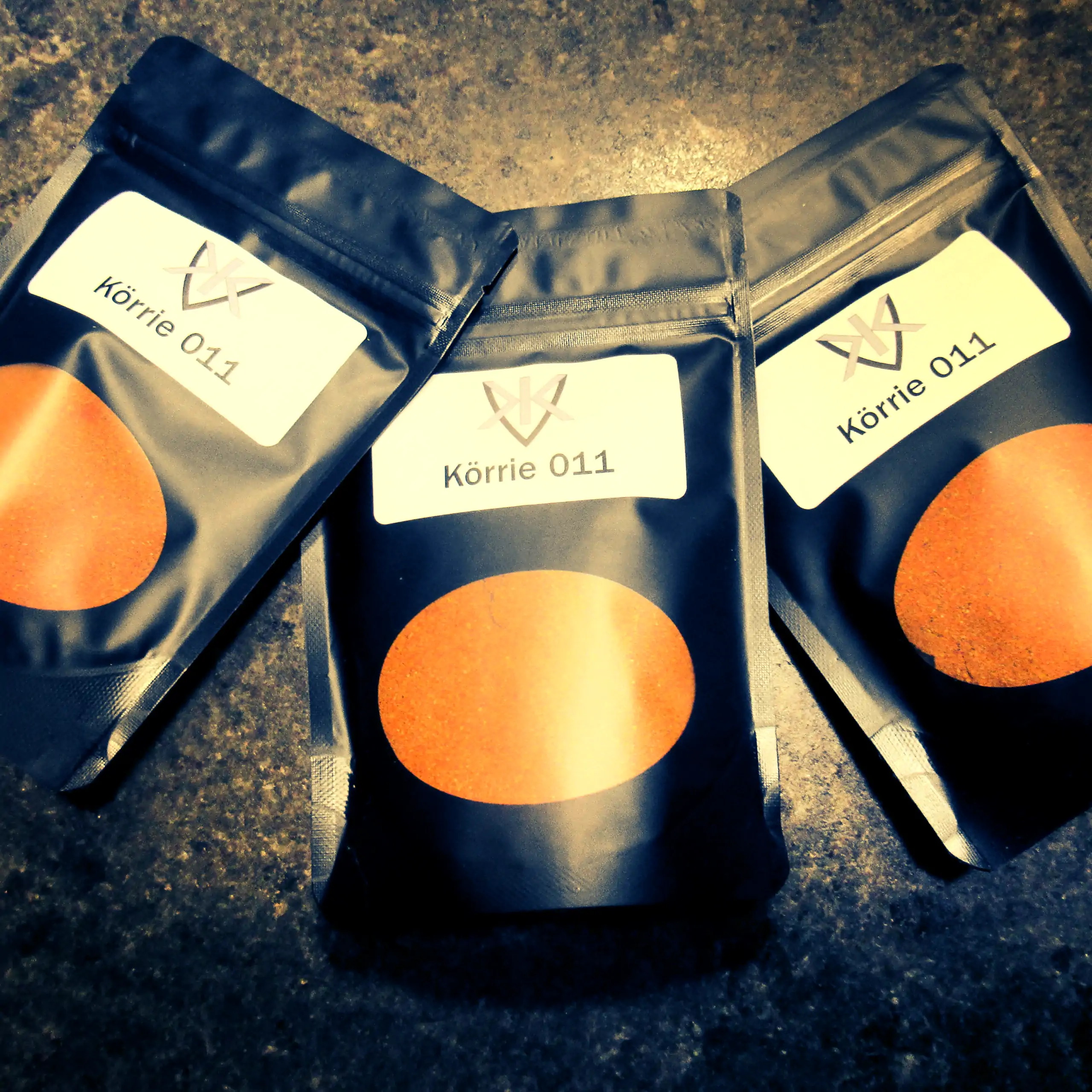 Alternatives Vorschaubild der Galerie für Körrie 011 Gewürzmischung: Drei schwarze Beutel mit transparentem Sichtfenster, durch das die leuchtend orange-rote, fein gemahlene, rauchig-scharfe Currypulver-Mischung sichtbar ist, versehen mit weißen Labels, d