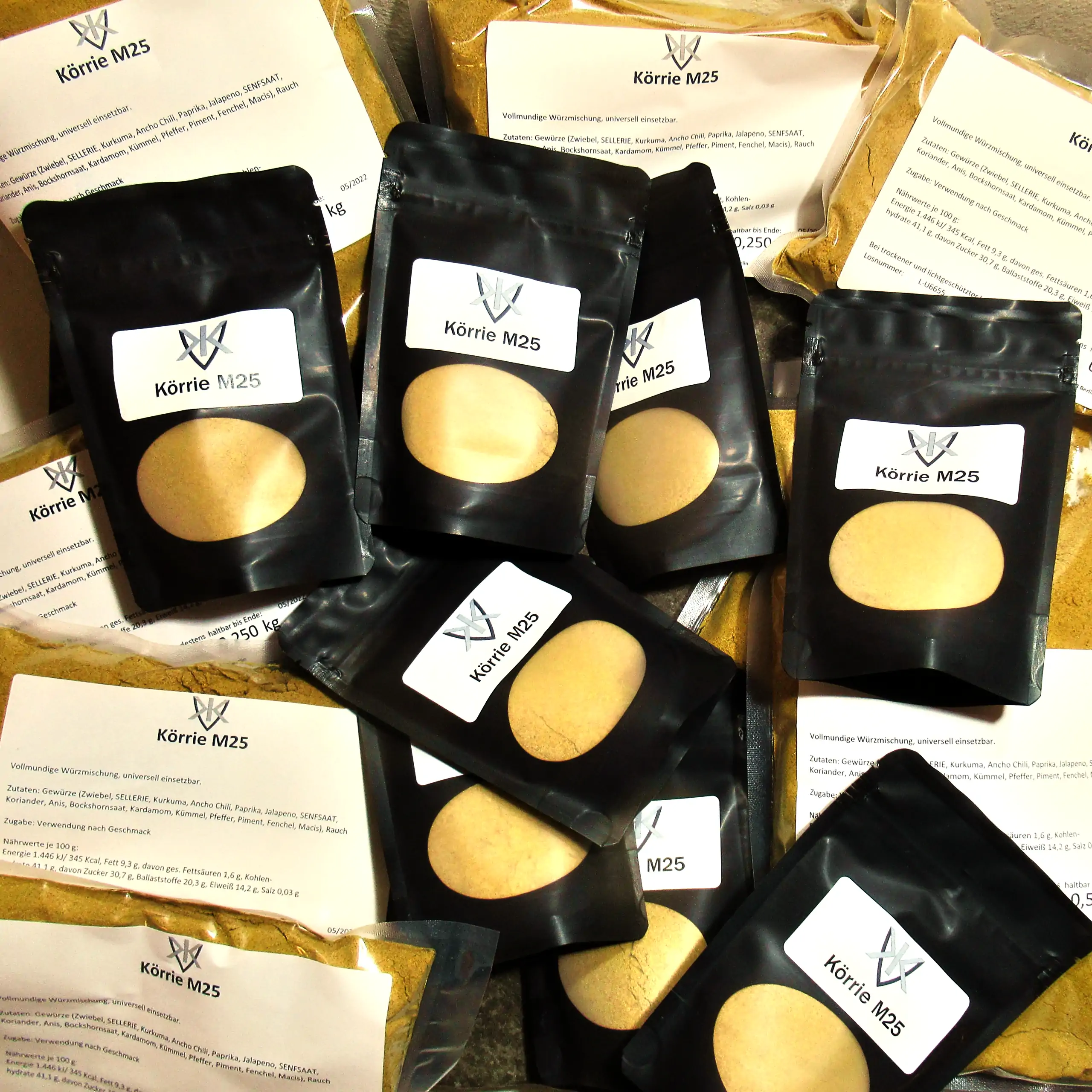 Detailaufnahme der Körrie M25 Gewürzmischung: Eine Sammlung schwarzer Beutel mit transparentem Sichtfenster, durch das die leuchtend goldgelbe, fein gemahlene vollmundige Würzmischung sichtbar ist, versehen mit weißen Labels "Körrie M25" und dem Logo von 