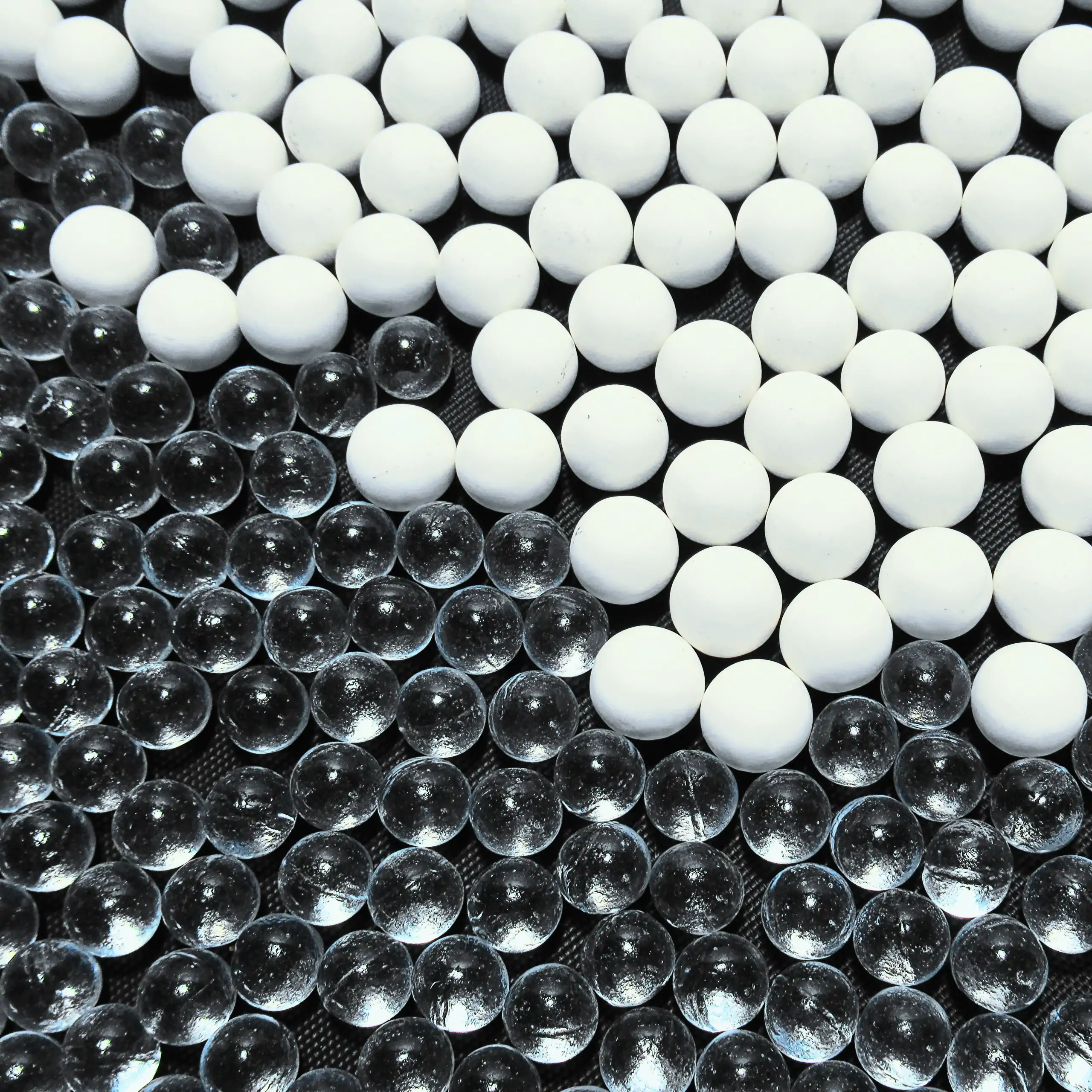 Extra Bild der Körrie-Aktiv-Perlen aus Glas (Körrie KAP L): Eine Mischung aus leuchtend transparenten, glänzenden, gehärteten Glasperlen und weißen matten Keramikperlen (Körrie KAP S), verstreut auf einer dunklen Oberfläche mit funkelnden Lichtreflexen fü