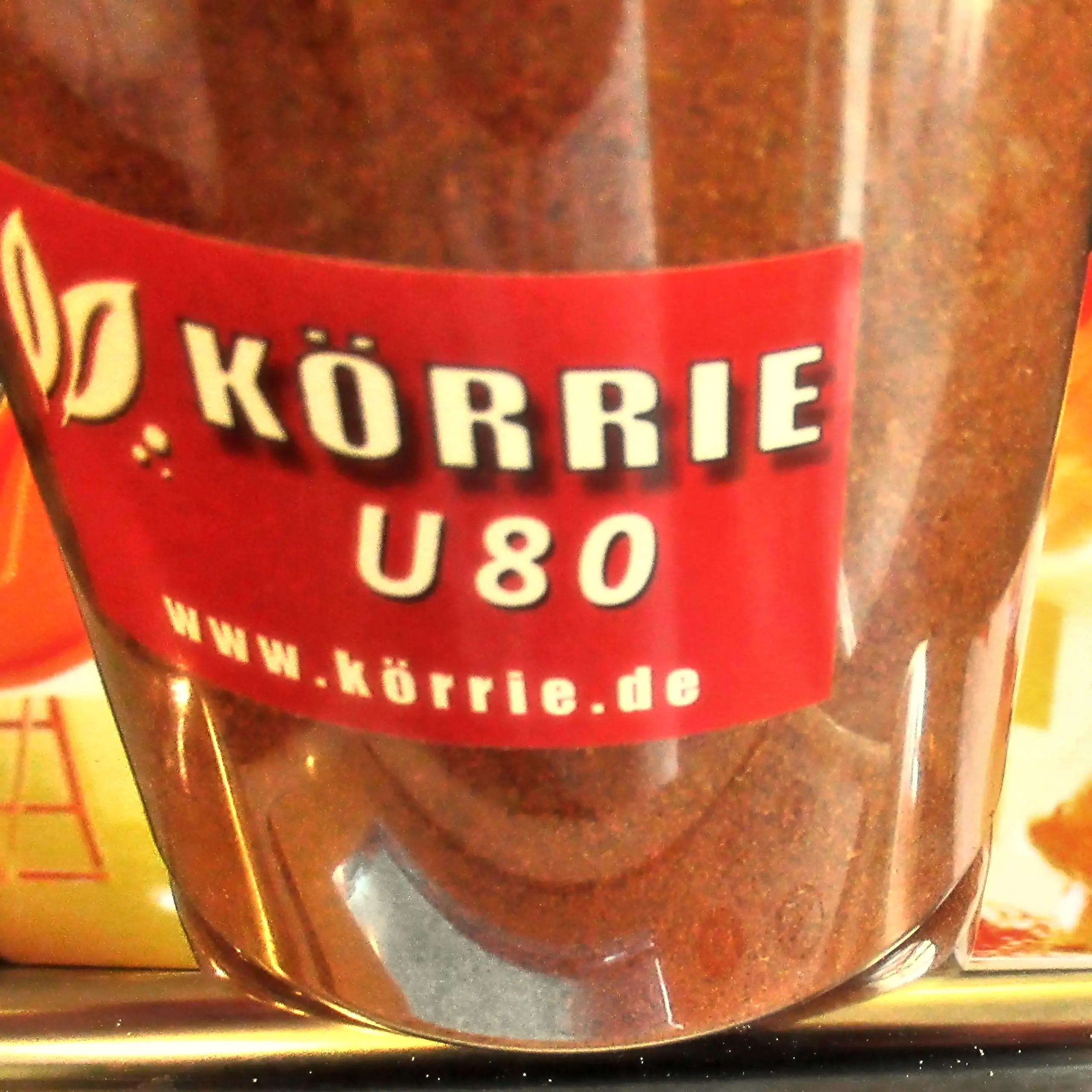 Alternatives Vorschaubild der Galerie der Körrie U80 Gewürzmischung: Eine rote Dose mit transparentem Körper, durch den die leuchtend rot-orangene, fein gemahlene, scharfe Gewürzmischung sichtbar ist, versehen mit einem roten Label, das ein Blätter-Logo, 