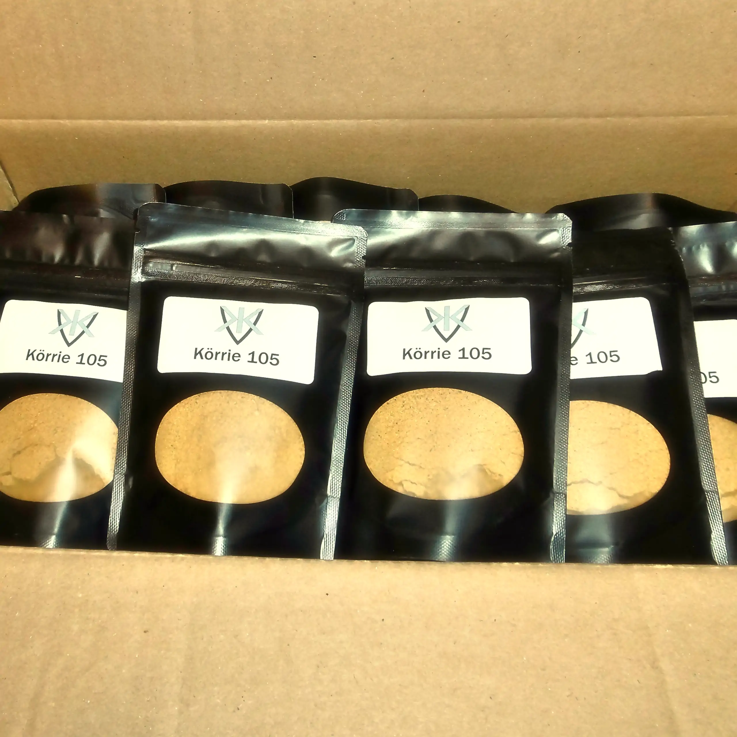 Zusätzliches Bild der Körrie 105 Gewürzmischung: Eine Kartonbox gefüllt mit mehreren schwarzen Beuteln, durch transparente Sichtfenster die leuchtend goldgelbe, fein gemahlene Currypulver-Mischung sichtbar, versehen mit weißen Labels "Körrie 105" und dem 