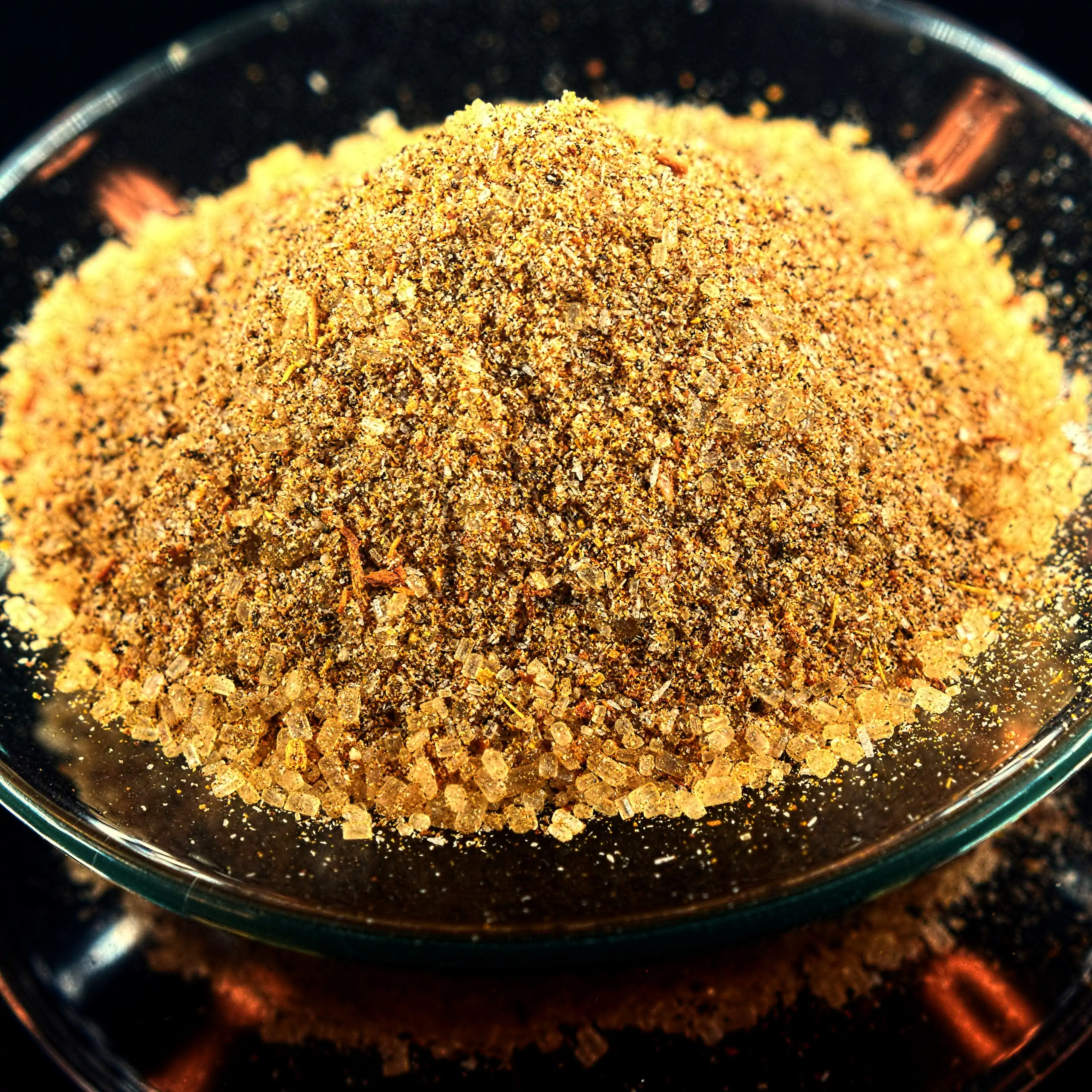 Zusätzliches Bild der Körrie WVZ Mischung: Ein Haufen leuchtend goldbrauner, fein gemahlener würzig-süßer Mischung mit strukturiert erkennbaren Kristallen von Rohrzucker in einer transparenten Glasschale auf dunklem Hintergrund mit goldenen Reflexen, die 