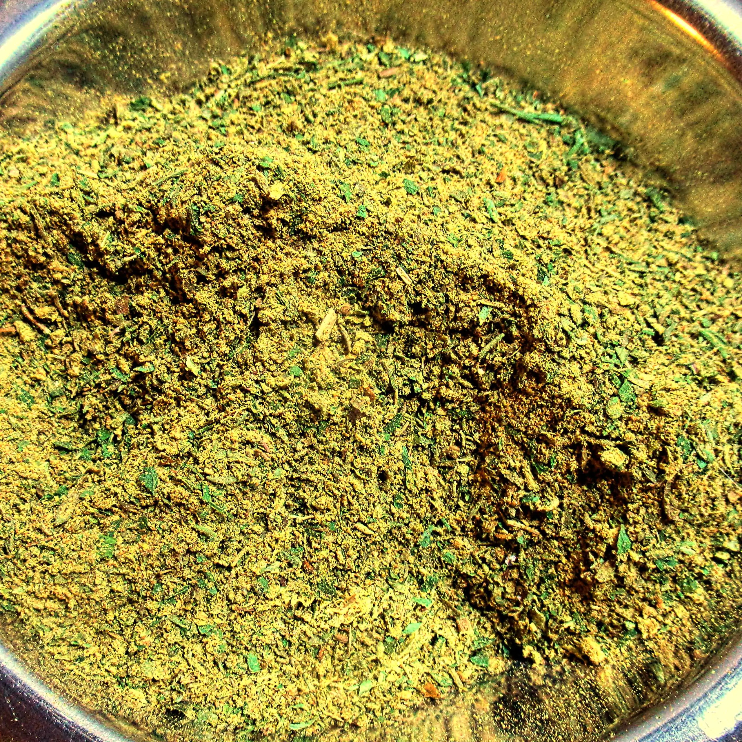 Ergänzende Ansicht des Körrie 4x4 (Kräuter- und Gewürzmischung): Ein Haufen leuchtend grüner, grob gemahlener würziger Mischung mit erkennbaren Feinanteilen in einer reflektierenden Edelstahlschale auf dunklem Hintergrund, die natürliche Textur aus Blätte