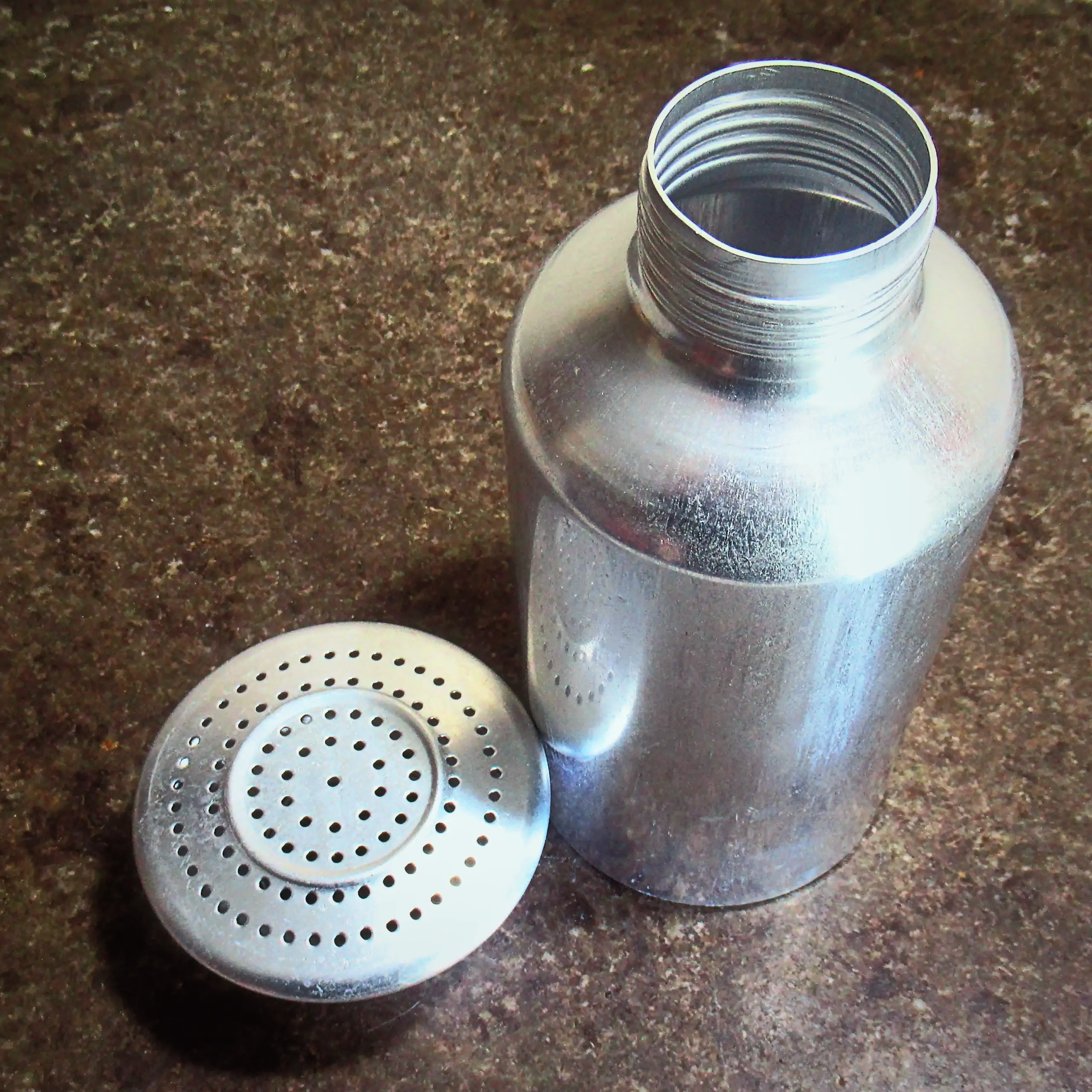 Alternatives Vorschaubild der Galerie für Körrie-Gewürz-Streuer / Körrie KGS: Ein robuster, silberfarbener Metallstreuer mit perforiertem Deckel für präzise Dosierung, offen präsentiert mit dem Deckel daneben auf einer rustikalen seidenmatt polierten Natu