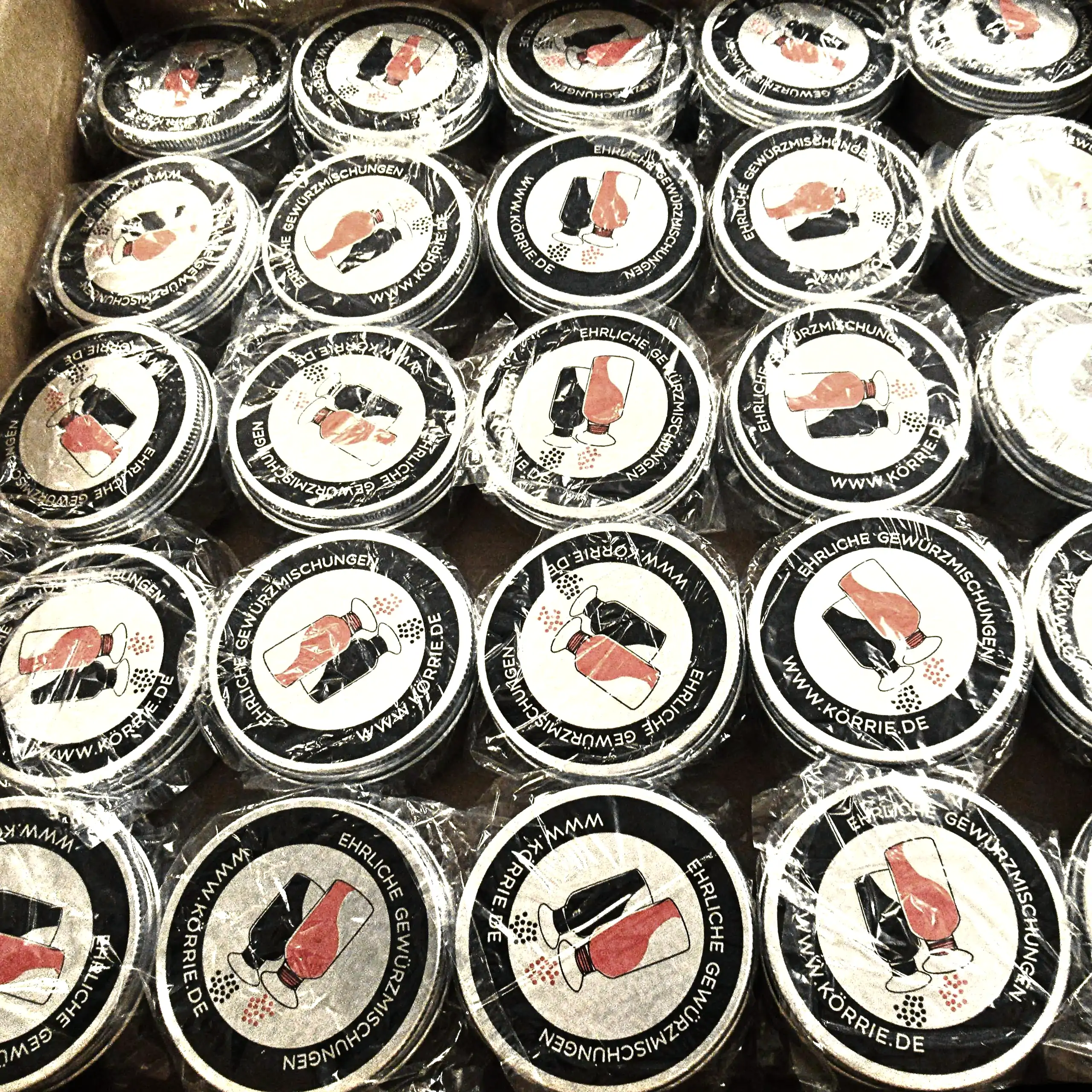 Zusätzliches Bild der Körrie-Support-Dose: Eine Kartonbox gefüllt mit zahlreichen, eingelagerten Metall-Dosen Körrie KSD mit bedruckten Deckeln, versandbereit verpackt in schützender Folie. Die Deckel tragen das ikonische Logo von Körrie mit den zwei Stre