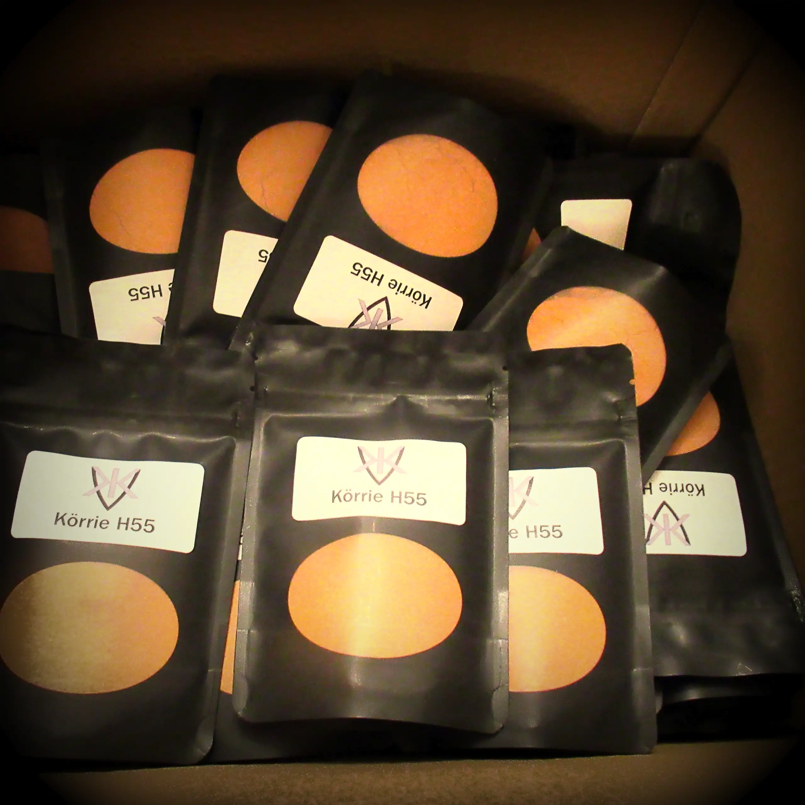 Alternatives Vorschaubild der Galerie für Körrie H55 Gewürzmischung: Ein Stapel schwarzer Beutel mit transparentem Sichtfenster, durch das die leuchtend orange-rote, fein gemahlene herzhafte Gewürzmischung sichtbar ist, versehen mit weißen Labels, die das